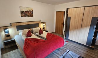A modern bedroom with a double bed and red decorative pillows. The room has a warm wood look and is well lit.