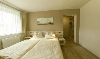 A bright bedroom with a large bed and decorative pillows. The room has large windows and a wardrobe for storage.