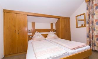 A simple bedroom with two single beds and wooden furniture. There is a mirror and a curtain with a colorful pattern.