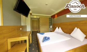 A modern guest room with wooden furniture and a television. There are two beds that are neatly made, as well as a table and chairs.