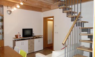 A modern living room with a staircase, a television, and a dining table. The walls are bright and the furnishings are simple and stylish.