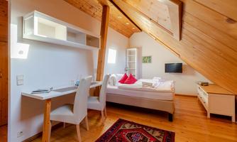 A cozy bedroom with a wooden ceiling and a bed. There is a desk, a television, and an oriental carpet.