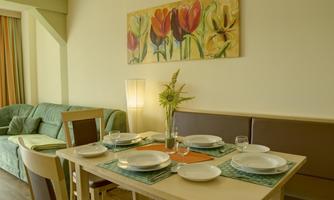 A cozy dining area with a table that is neatly set. In the background, a green couch and a colorful flower painting can be seen.