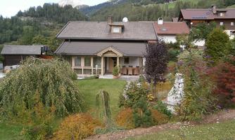 A cozy house with a well-maintained garden and colorful bushes. In the background, green hills and trees can be seen.