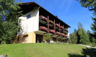 A cozy building with several balconies adorned with colorful flowers. Surrounded by green nature and trees.