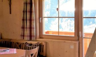 A cozy room with wooden furniture and a large window that offers a view of the mountains. A table is set for a meal.