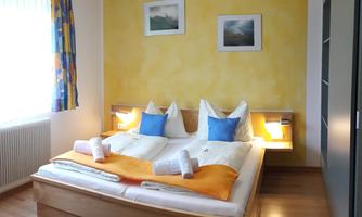 A modern bedroom with a large double bed. The walls are painted yellow and there are light sources next to the bed.