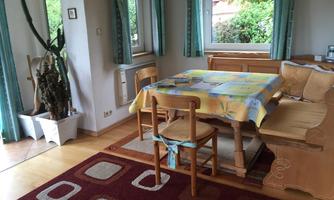 A cozy dining area with a wooden table and chairs. The room has large windows and an inviting atmosphere.
