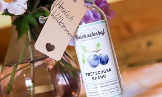 A bottle of plum brandy stands next to a bouquet of flowers in a glass vase. The background is cozy and rustic.