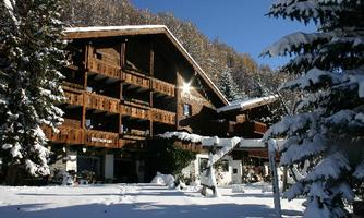A cozy wooden building in winter, surrounded by snow-covered trees. The sun shines on the peaceful winter landscape.