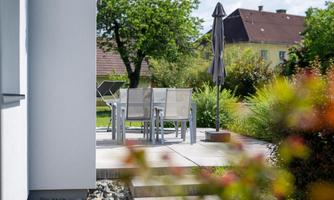 A cozy outdoor area with a table and four chairs. A sunshade provides shade in a green environment.