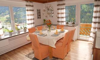 A cozy dining area with a large table and orange chairs. View of the surrounding nature through large windows.