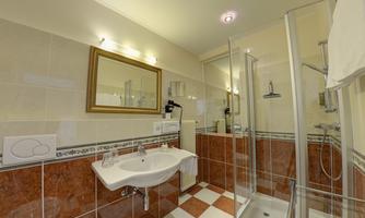 A modern bathroom with a shower, sink, and a large mirror. The walls are tiled in light colors and the floor has a checkered pattern.