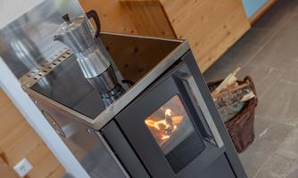 A modern stove with boiling water in a coffee pot. Next to it is a basket with wood.