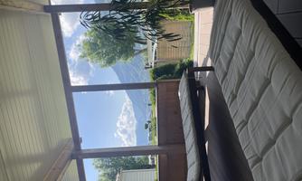 A cozy terrace with loungers and a view of green landscapes and mountains. The sky is clear with a few clouds.