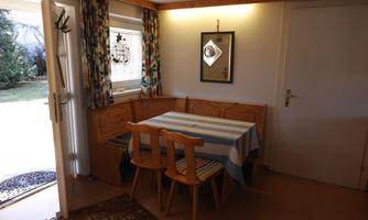 A cozy dining area with a wooden table and chairs. The window lets in a lot of light and offers a view of the garden.