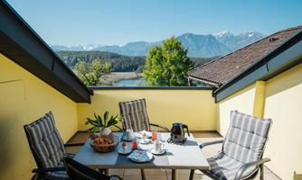 A cozy terrace with a table and chairs. In the background, mountains and a clear sky are visible.