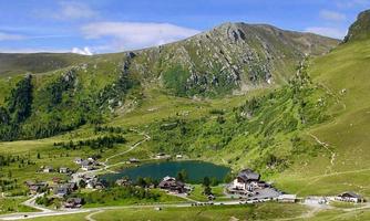 A picturesque mountain landscape with a clear lake and small cottages. The surroundings are green and surrounded by majestic mountains.
