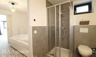 A modern bathroom with a shower and bright tiles. In the background, a bed and a door are visible.