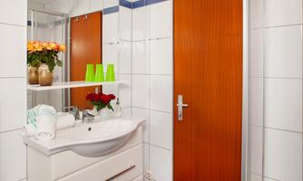 A modern bathroom with a white washbasin and a mirror. Fresh flowers and colorful decorative items are on the shelf.