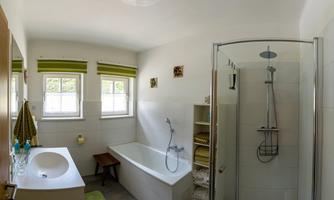 A modern bathroom with a bathtub and a separate shower. There are windows that let in bright daylight, and shelves with towels.