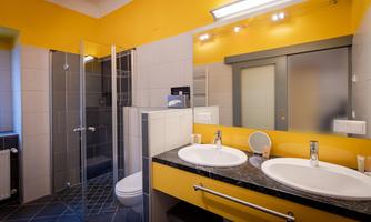 A modern bathroom with orange walls and a glass shower. There is a double sink and large mirrors above the countertop.