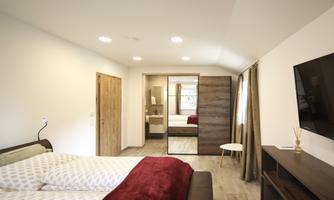A modern bedroom with a large bed and cozy bedding. The room features a television, a mirror, and a small table.