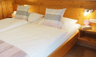 A cozy bedroom with a double bed and two decorative pillows. The walls are made of wood, creating a warm atmosphere.