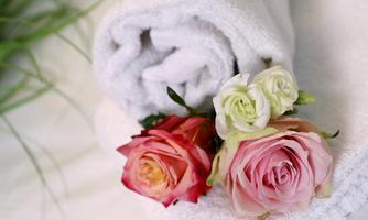 A white towel is rolled up and lies on a surface. Next to the towel are three fresh roses in different colors.