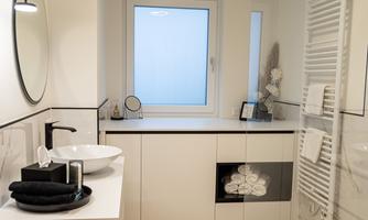 A modern bathroom with elegant furniture and bright light. The room is clean and well-organized, with a large mirror and a window front.