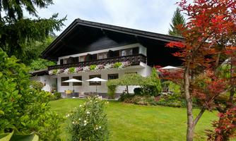 A beautiful house with a well-maintained garden. In the foreground, colorful plants and umbrellas can be seen.
