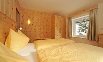 A cozy bedroom with wooden paneling and two single beds. Large windows let in plenty of daylight and offer a view of nature.