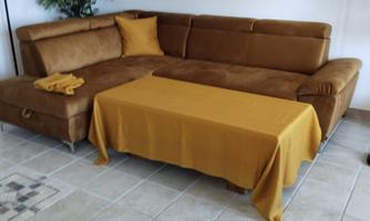 A cozy living room with a brown sofa and a yellow tablecloth. A picture of a forest landscape hangs on the wall.