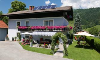 A beautiful two-story house with a colorful flower box and a garden. Surrounded by a well-maintained lawn and trees in an idyllic setting.