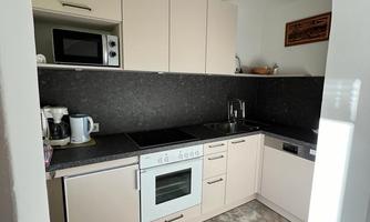 A modern kitchen with bright cabinets and black countertops. The equipment includes a stove, a refrigerator, and a microwave.