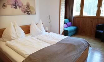 A cozy bedroom with a double bed and two pillows. Next to the bed is an armchair and a large window with a view to the outside.