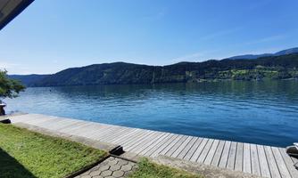 A calm water surface with gentle hills in the background. The dock and the grass in the foreground create a relaxed atmosphere.