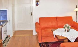 A cozy living room with an orange sofa and a small table. The room has a bright floor and a white wall, creating an inviting atmosphere.