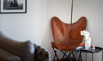 An elegant brown butterfly chair in a bright corner of the room. Next to the chair stands a table with a flower and a candle.