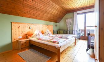 A cozy bedroom with wooden walls and a double bed. Large windows provide plenty of light and a view.
