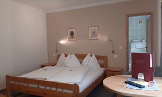 A cozy room with a double bed and bright walls. Next to the bed is a table with a drink and a menu.