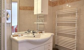 A modern bathroom with a sink, a mirror, and towel racks. The walls are brightly tiled, and there is a shower area.
