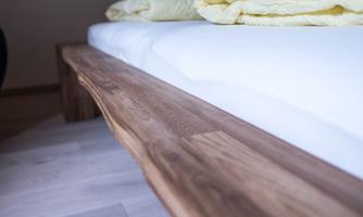 A wooden bench next to a bed with a white mattress. Yellow blankets are laid over it.