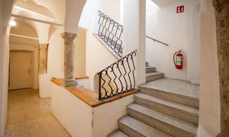 A bright interior with a staircase and a wrought-iron railing. A fire extinguisher hangs on the wall for safety.