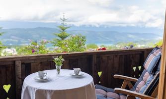 A cozy balcony with a view of the mountains. On the table are two cups and a vase with flowers.