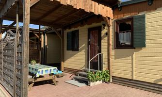 A cozy holiday home with a veranda and an outdoor table. The facade is designed in warm colors and there are windows with green shutters.