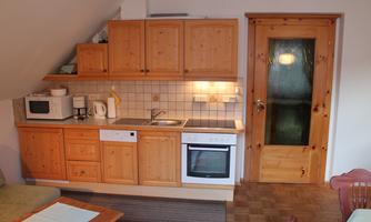 A cozy kitchen with wooden cabinets, a stove, and a microwave. The door has a glass window and the decor feels warm and inviting.
