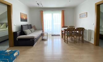 A bright and cozy living room with a sofa and a dining table. Large windows provide plenty of daylight.