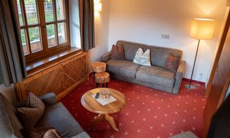 A cozy living space with a gray sofa and two beige armchairs. A round table sits in the center, and large windows let in plenty of daylight.