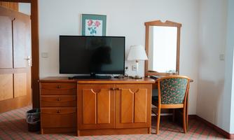 A simple hotel room with wooden furniture. A television, a desk with a chair, and a mirror are clearly visible.